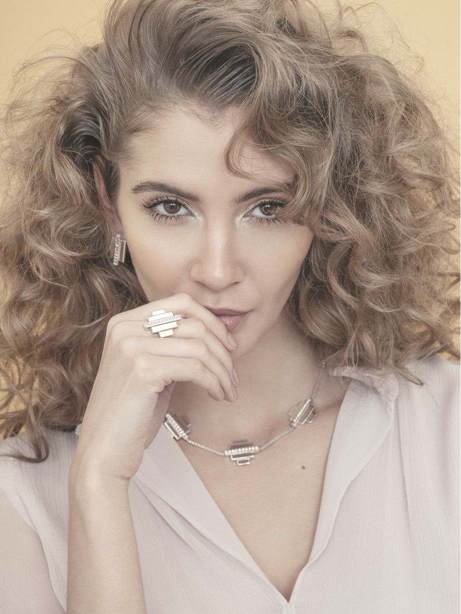 Mulher com cabelo encaracolado usando anel inca prata Topázio 1874 em destaque, acompanhada de colar e brincos de prata