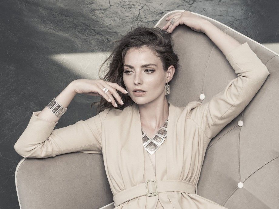 Mulher elegante reclinada usando brincos hedra prata feminina da Carmo Joalheiros com colar e anel