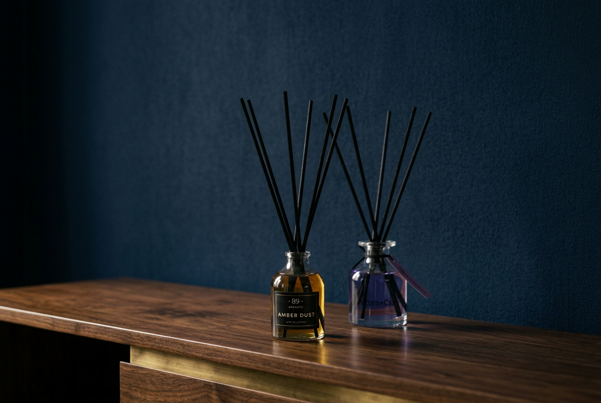 Difusores de varetas AROMATIC•89• e Agnes + Cat numa composição com fundo azul-marinho e madeira escura.