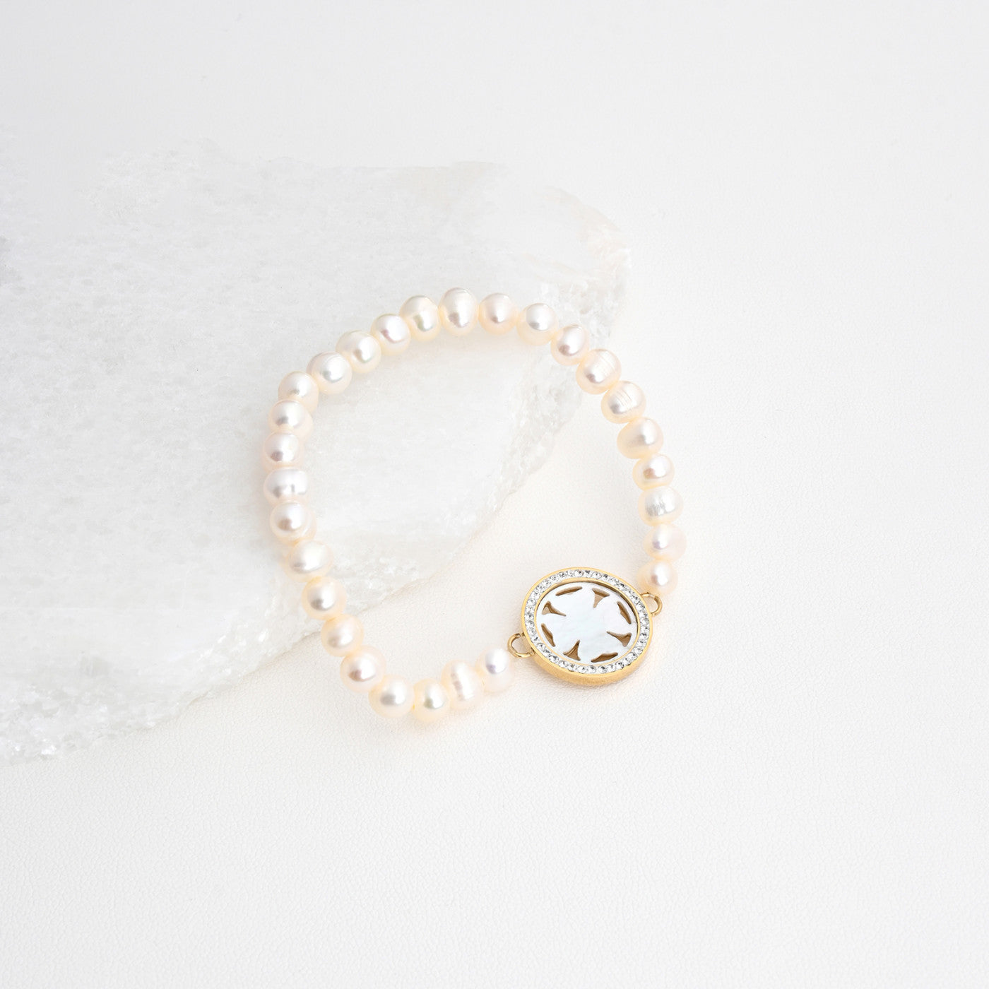 pulseira de aço com pérolas Carmo Joalheiros joia de pérolas com medalhão dourado e esmalte branco em fundo neutro