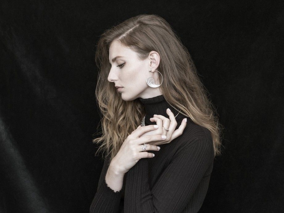 Mulher com cabelo ondulado a usar anel filigrana portuguesa da Topázio 1874 e brincos prateados em fundo negro