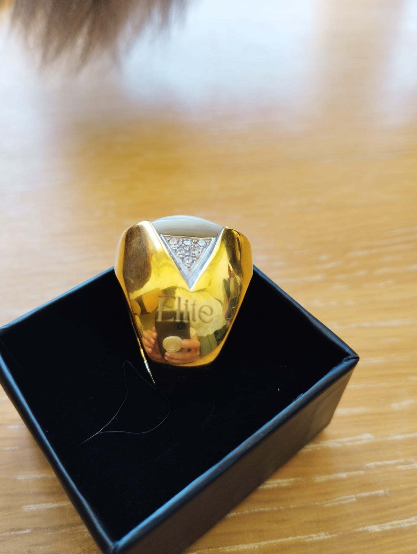 anel madrepérola feminino ELITE dourado com madrepérola central e detalhe triangular de cristais em caixa preta sobre madeira