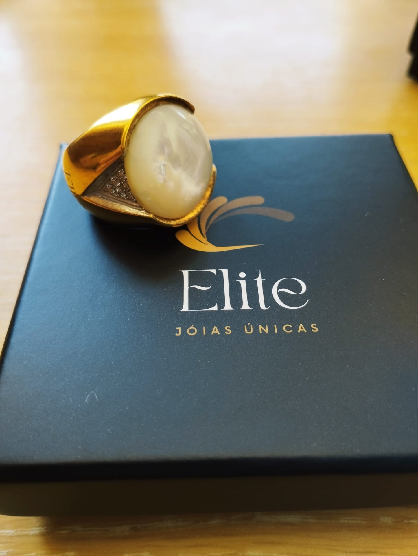 anel madrepérola feminino ELITE dourado com pedra oval e detalhes em zircônia sobre estojo preto