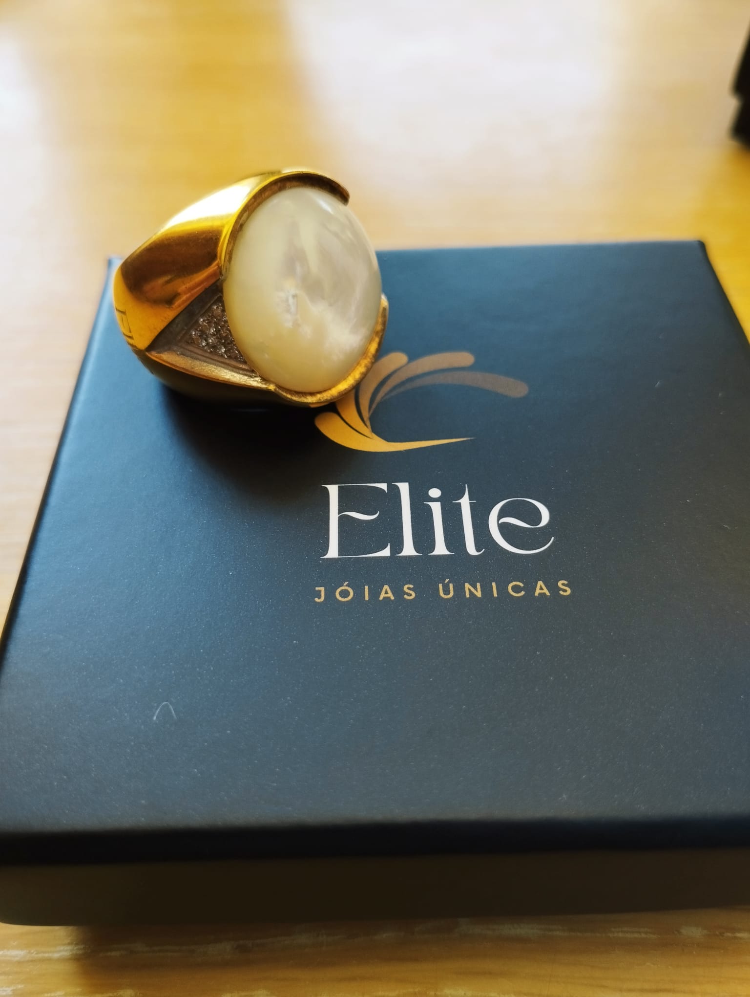 anel madrepérola feminino ELITE dourado com pedra oval e detalhes em zircônia sobre estojo preto