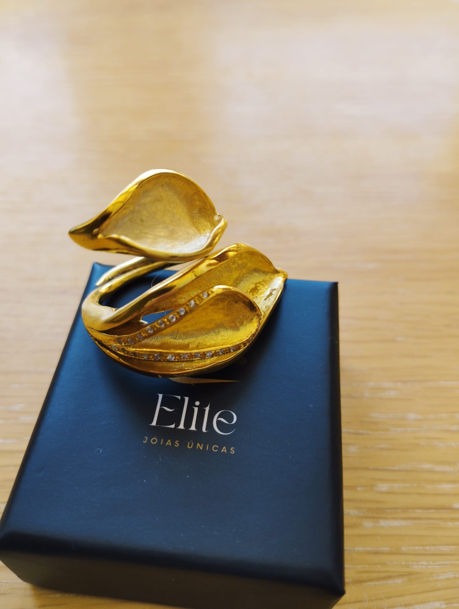 Joia Exclusiva Elite anel de ouro Lirio da Paz anel dourado em formato lirio com detalhes cravejados sobre caixa Elite