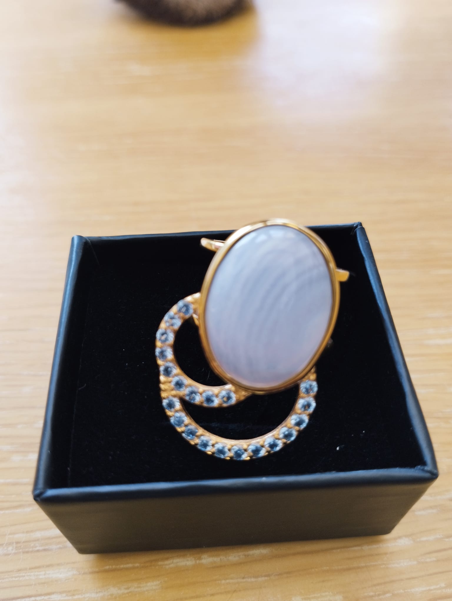 Joia Exclusiva Elite anel de luxo Moon Acquamarina mostrada em caixa preta, aro dourado com pedra oval e detalhes cravejados