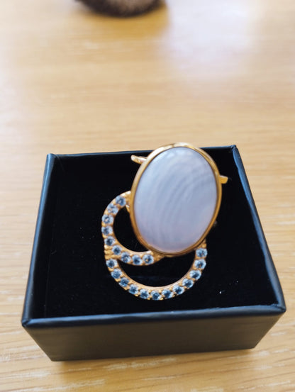 Joia Exclusiva Elite anel de luxo Moon Acquamarina mostrada em caixa preta, aro dourado com pedra oval e detalhes cravejados