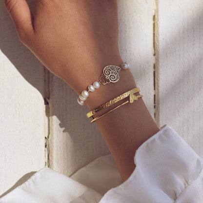 Carmo Joalheiros pulseira de pérolas com coração de Viana mostrada no pulso com braceletes dourados elegantes