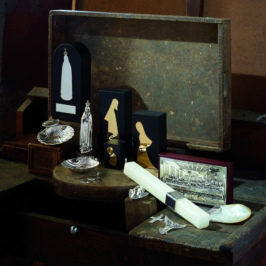 Display de joalharia Carmo Joalheiros com bibelot Nossa Senhora de Fátima dourado e vela artesanal sobre caixa e conchas